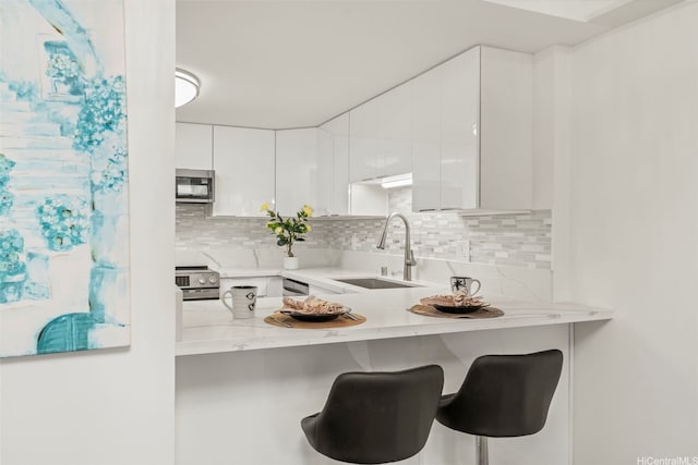 1433 Kewalo St Unit Ph12, Honolulu, HI 96822 - kitchen with a kitchen breakfast bar, white cabinetry, backsplash, appliances with stainless steel finishes, and a sink