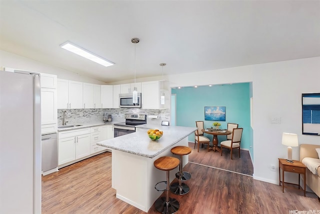 kitchen with a peninsula, appliances with stainless steel finishes, wood finished floors, a sink, and lofted ceiling