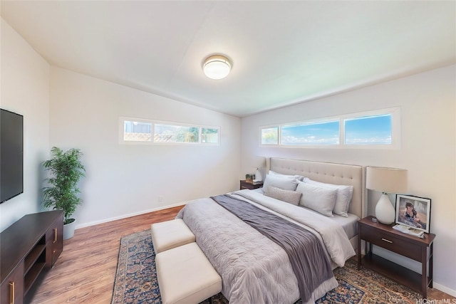 bedroom featuring baseboards, light wood-type flooring, and vaulted ceiling
