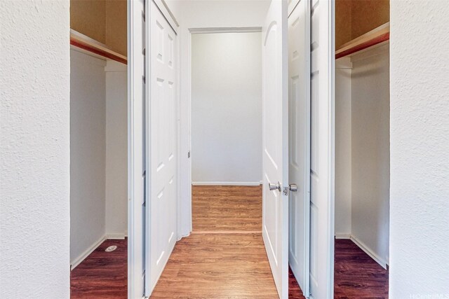 hall with a textured wall, baseboards, and wood finished floors