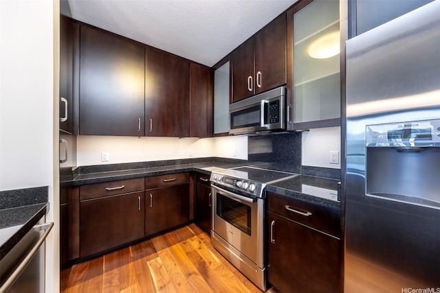 1189 Waimanu St Unit 2803, Honolulu, HI 96814 - kitchen with appliances with stainless steel finishes, light wood finished floors, glass insert cabinets, dark brown cabinetry, and dark stone countertops