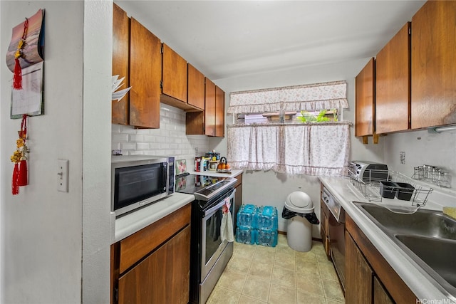 kitchen featuring backsplash, brown cabinets, a sink, light countertops, and stainless steel appliances