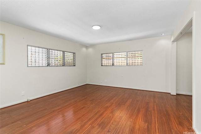 empty room featuring wood finished floors, healthy amount of natural light, and baseboards