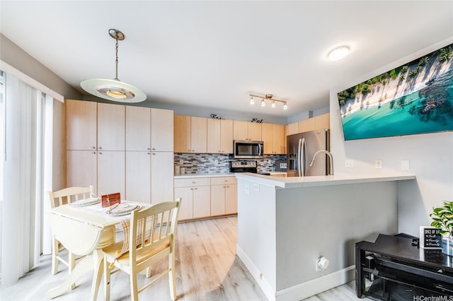 kitchen with a peninsula, light brown cabinetry, light countertops, tasteful backsplash, and appliances with stainless steel finishes
