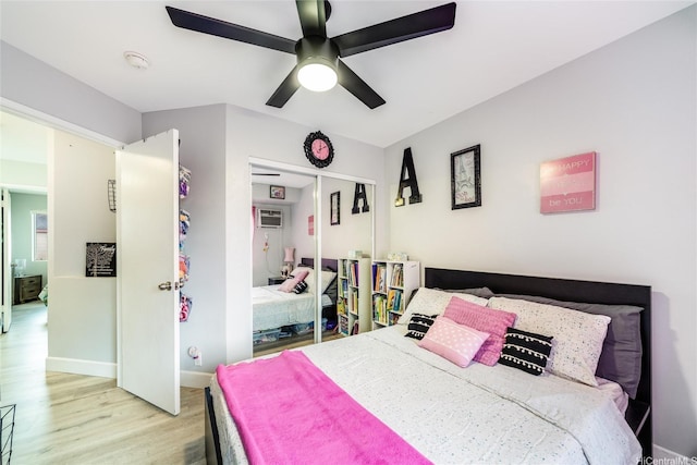 bedroom with a closet, baseboards, a wall unit AC, a ceiling fan, and light wood finished floors