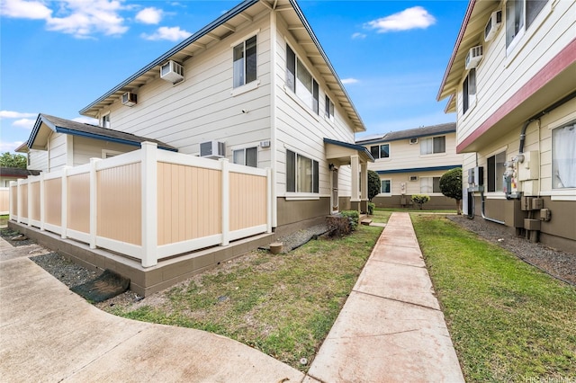 view of side of property with fence, central AC unit, a wall unit AC, and a yard