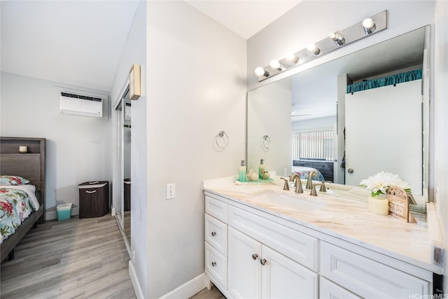 full bathroom with a wall mounted AC, wood finished floors, baseboards, vanity, and ensuite bath