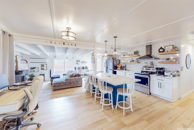 kitchen with open shelves, light wood-style flooring, appliances with stainless steel finishes, and wall chimney range hood