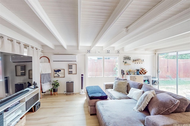 living area with light wood-type flooring, baseboards, a wall unit AC, and beam ceiling