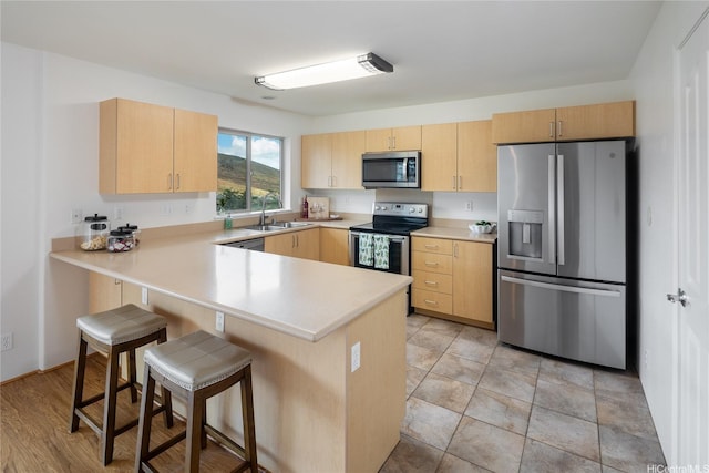 92-1199 Pueonani St, Kapolei, HI 96707 - kitchen with appliances with stainless steel finishes, a sink, light brown cabinets, a breakfast bar, and a peninsula