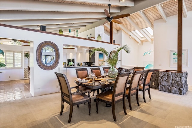 carpeted dining area featuring a skylight, high vaulted ceiling, beamed ceiling, and a ceiling fan