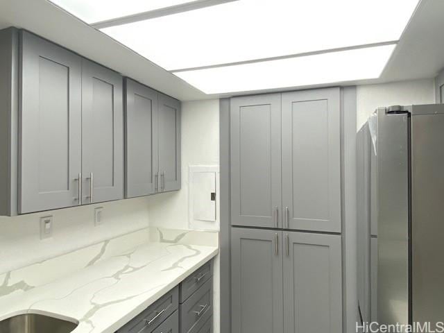 kitchen featuring freestanding refrigerator, light stone countertops, and gray cabinetry