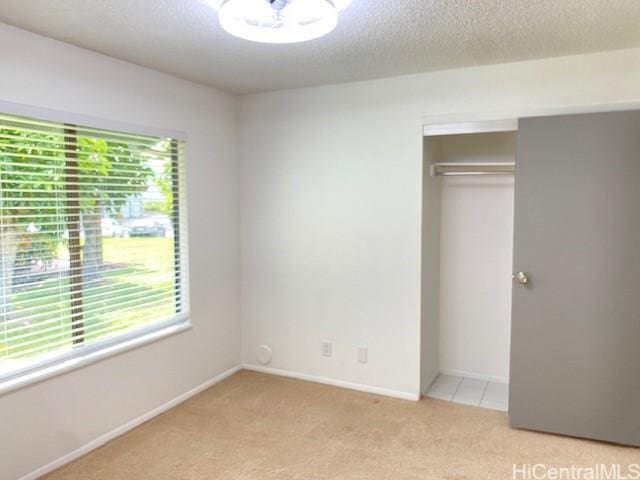 unfurnished bedroom with light carpet, a textured ceiling, a closet, and multiple windows