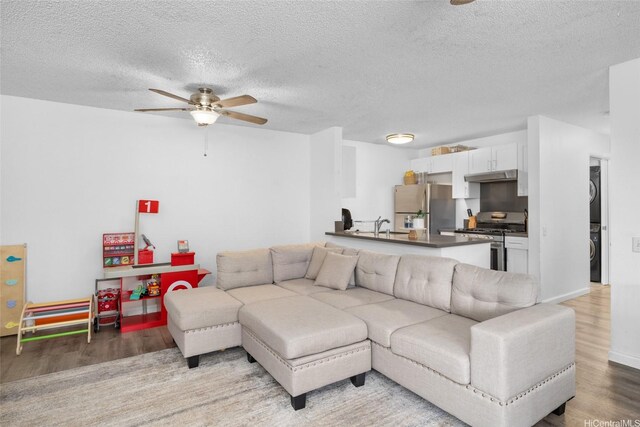 living room featuring stacked washer and clothes dryer, baseboards, a textured ceiling, a ceiling fan, and light wood-style flooring