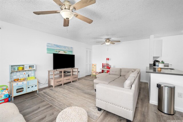 living area featuring baseboards, a ceiling fan, a textured ceiling, and wood finished floors