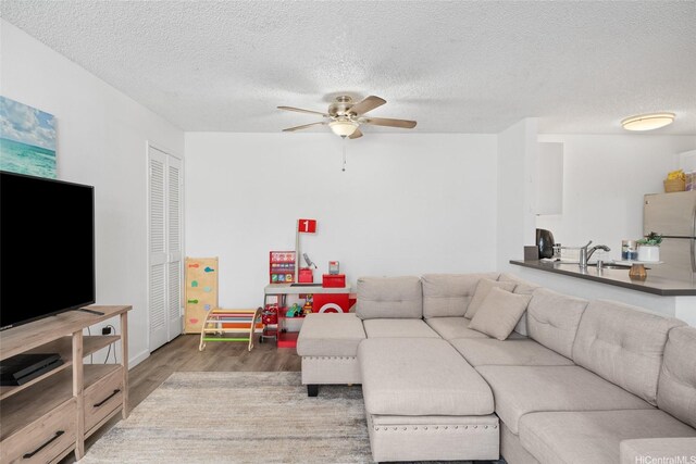 living area with a ceiling fan, a textured ceiling, and wood finished floors