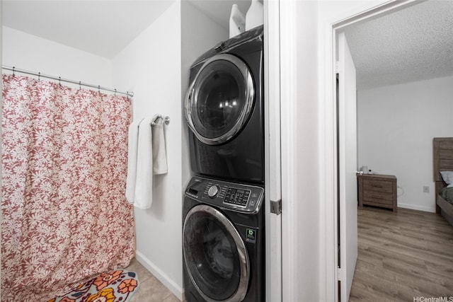 clothes washing area featuring laundry area, baseboards, stacked washer and clothes dryer, and wood finished floors