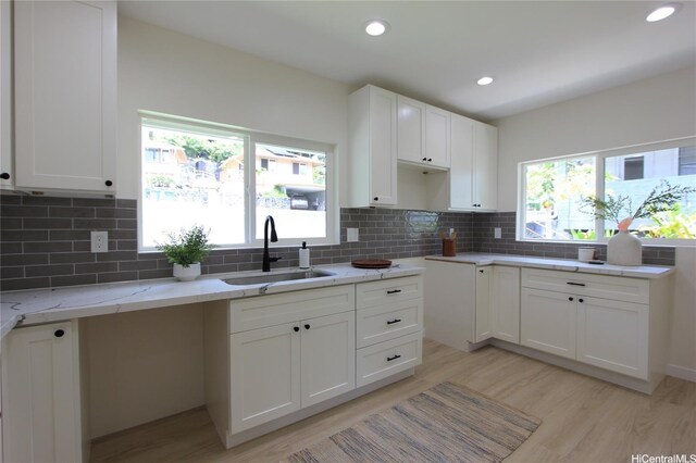 kitchen featuring light stone countertops, decorative backsplash, light wood-style flooring, and a sink