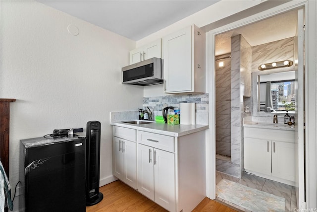 kitchen with stainless steel microwave, white cabinetry, a sink, and light countertops
