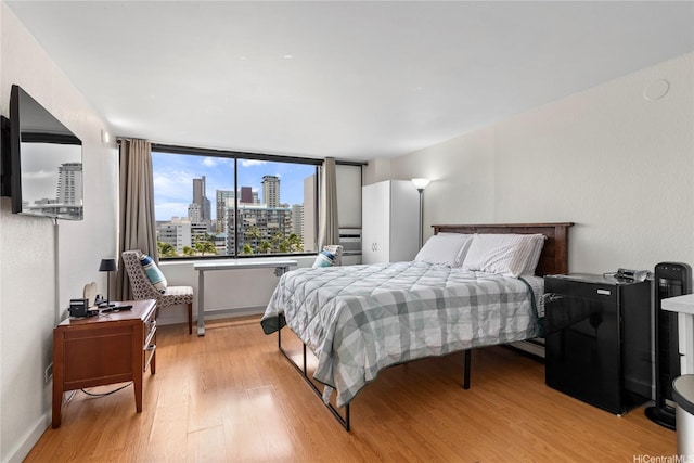 bedroom with light wood finished floors, baseboards, and a view of city