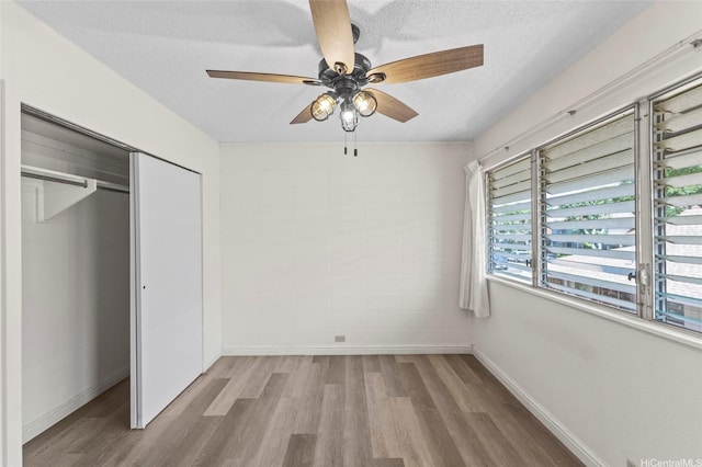 unfurnished bedroom featuring baseboards, wood finished floors, a textured ceiling, and a closet