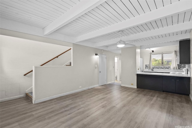 unfurnished living room featuring beamed ceiling, light wood-style floors, baseboards, stairs, and ceiling fan