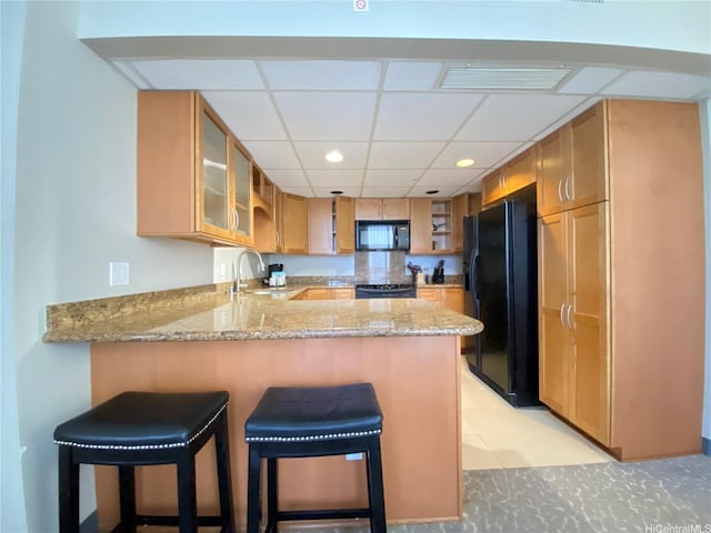 kitchen with light stone counters, a sink, black appliances, a peninsula, and visible vents