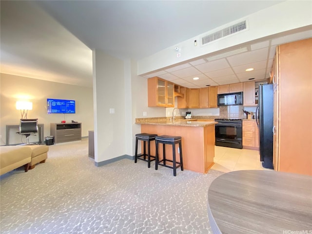 kitchen with a peninsula, a kitchen breakfast bar, a sink, visible vents, and black appliances