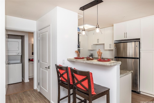 kitchen featuring freestanding refrigerator, white cabinets, stacked washer / drying machine, and wood finished floors