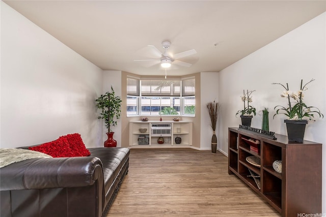 living area featuring light wood finished floors, baseboards, and a ceiling fan