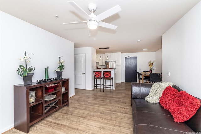 living area featuring light wood-style flooring, baseboards, and ceiling fan