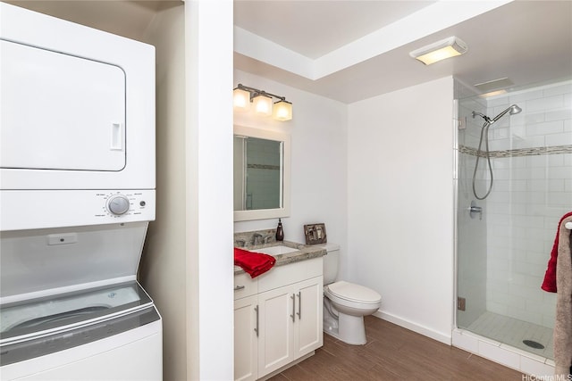 full bath featuring stacked washer and clothes dryer, toilet, wood finished floors, a shower stall, and vanity