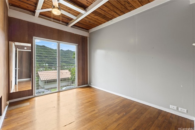 empty room featuring baseboards, beamed ceiling, a ceiling fan, wood finished floors, and wooden ceiling