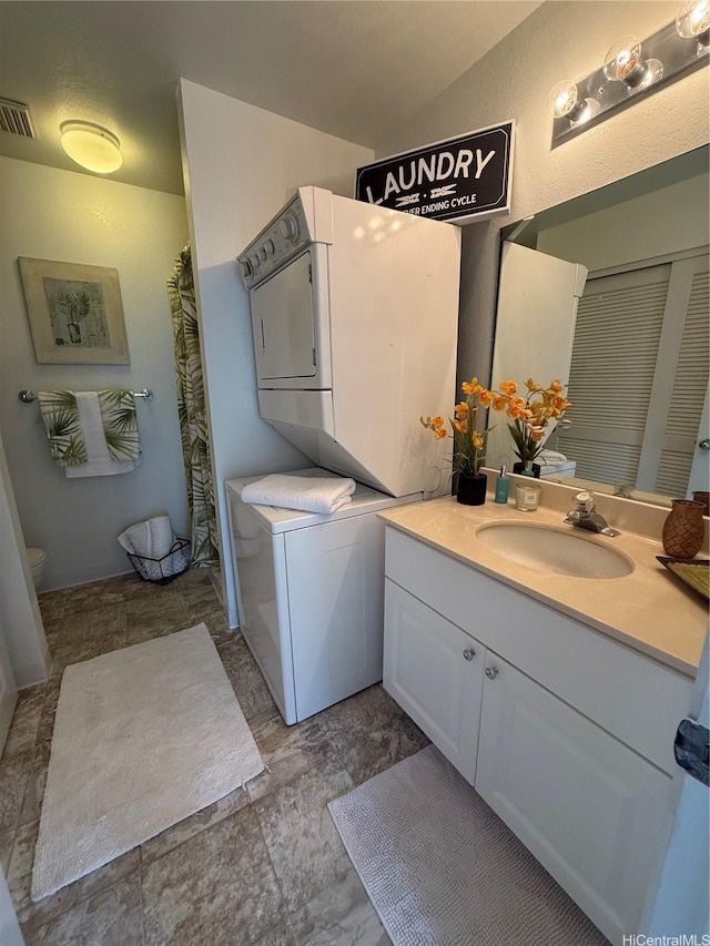 bathroom featuring stacked washer and dryer, visible vents, vanity, and toilet