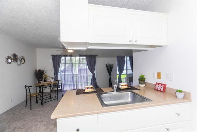 kitchen featuring a sink, a textured ceiling, carpet, a peninsula, and white cabinetry