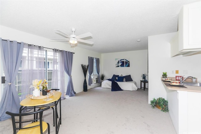 bedroom with a textured ceiling, a ceiling fan, light colored carpet, and a sink