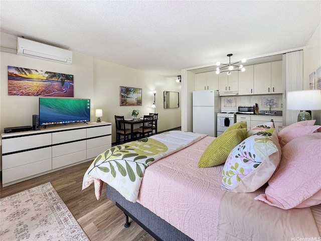 bedroom featuring a wall mounted air conditioner, wood finished floors, a textured ceiling, a notable chandelier, and freestanding refrigerator