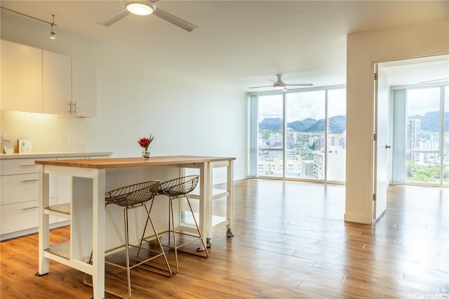 kitchen featuring white cabinets, a ceiling fan, a wall of windows, light wood-type flooring, and a breakfast bar area