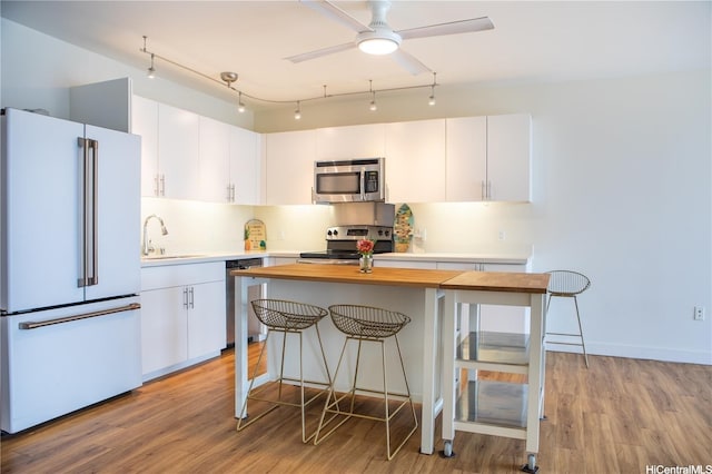 kitchen featuring white cabinets, a sink, a breakfast bar, wooden counters, and appliances with stainless steel finishes