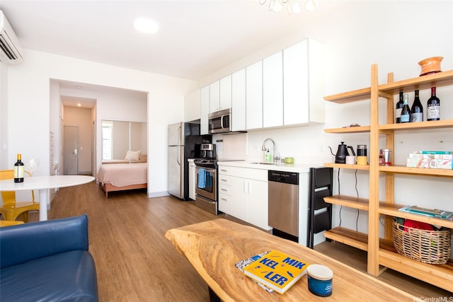 kitchen featuring a wall mounted air conditioner, wood finished floors, a sink, appliances with stainless steel finishes, and white cabinetry