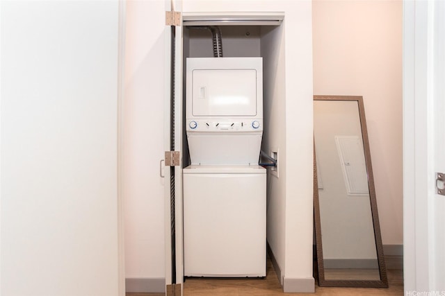 laundry area featuring baseboards, stacked washer / dryer, wood finished floors, and laundry area