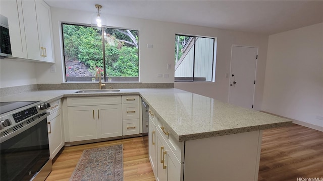 kitchen with white cabinets, stainless steel appliances, a sink, light stone countertops, and light wood-style flooring