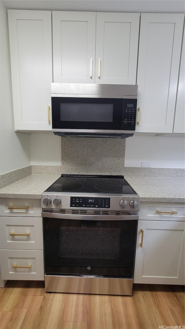 kitchen with white cabinetry, light stone countertops, stainless steel appliances, and light wood-style flooring