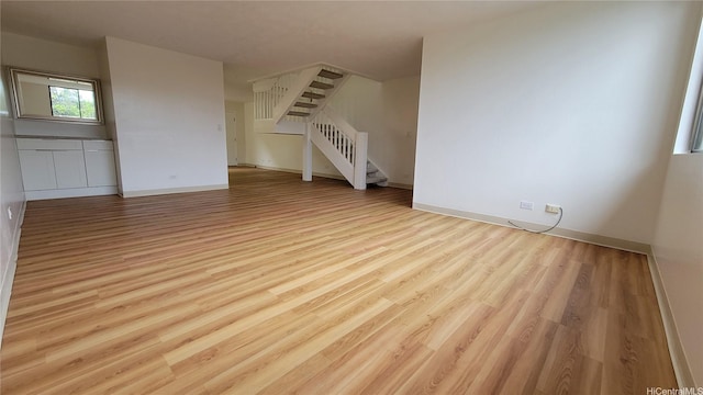 unfurnished living room featuring baseboards, wood finished floors, and stairs
