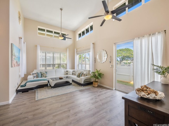 living area featuring ceiling fan, baseboards, wood finished floors, and a towering ceiling