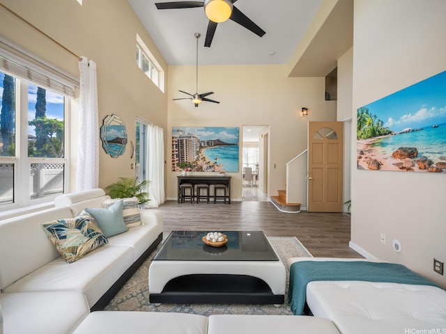 living area with wood finished floors, a wealth of natural light, a ceiling fan, and a towering ceiling