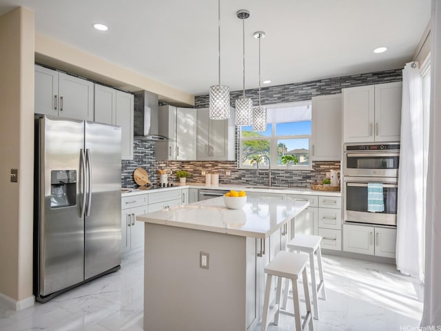 kitchen featuring a sink, marble finish floor, wall chimney range hood, a kitchen island, and appliances with stainless steel finishes