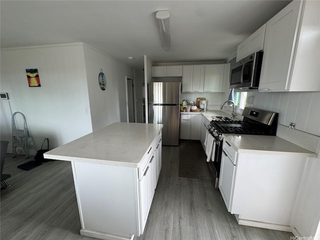 kitchen with a sink, stainless steel appliances, a kitchen island, light countertops, and wood finished floors