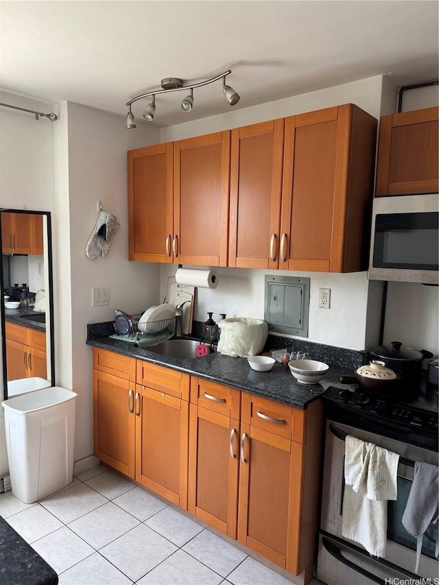 kitchen with dark stone counters, a sink, light tile patterned flooring, brown cabinetry, and appliances with stainless steel finishes