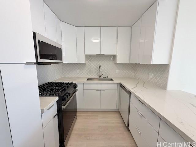 kitchen featuring stainless steel microwave, black gas range, white cabinetry, and a sink